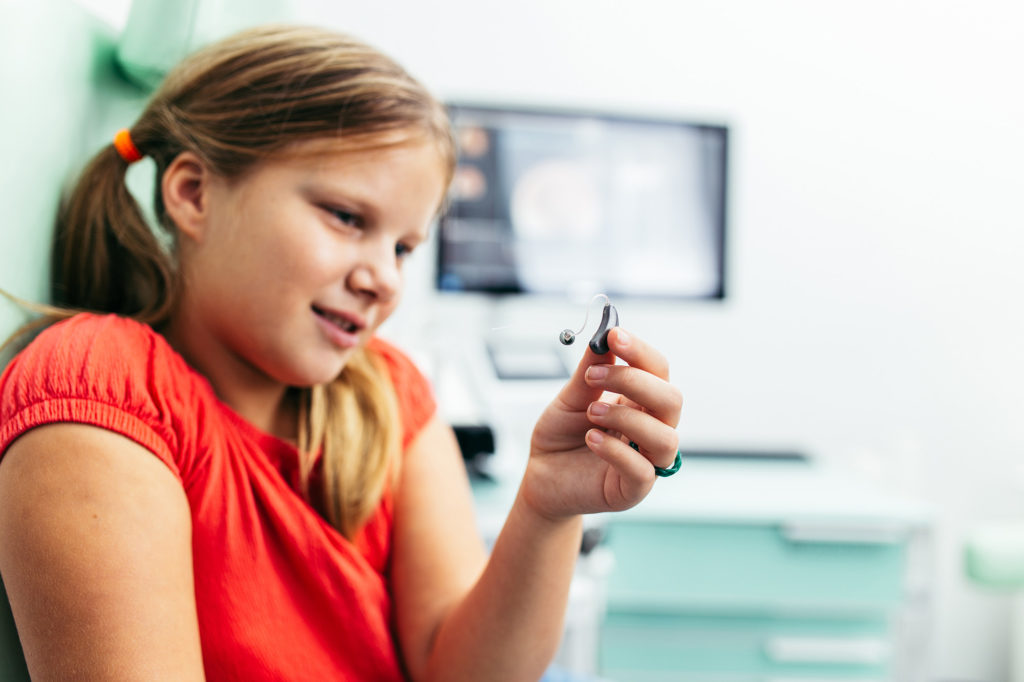 young girl holding up modern hearing aid